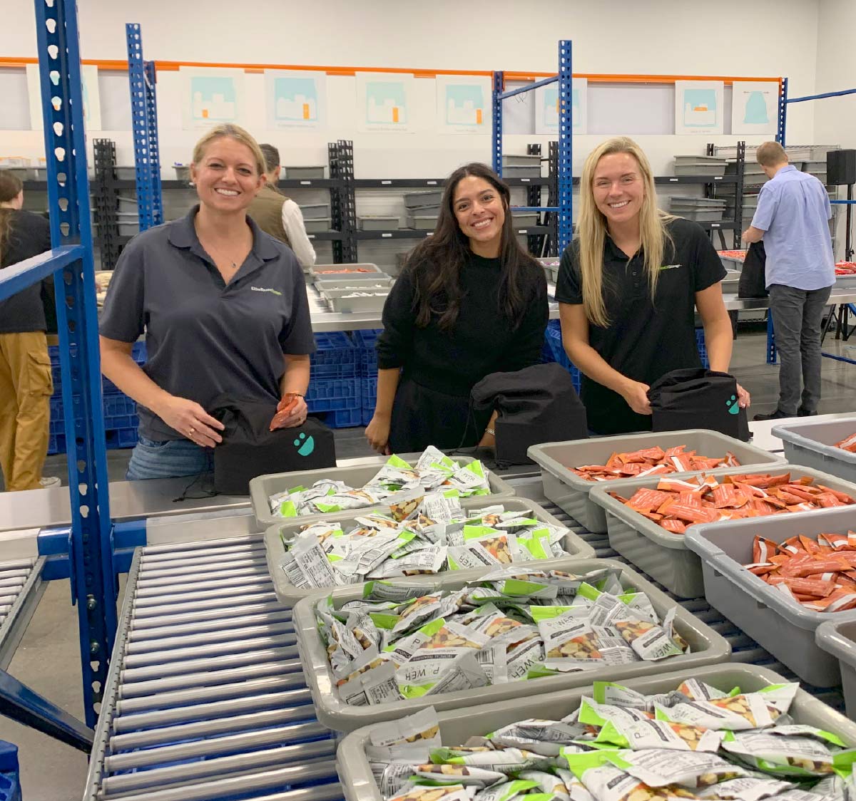 three women smiling while packing weekend backpacks 