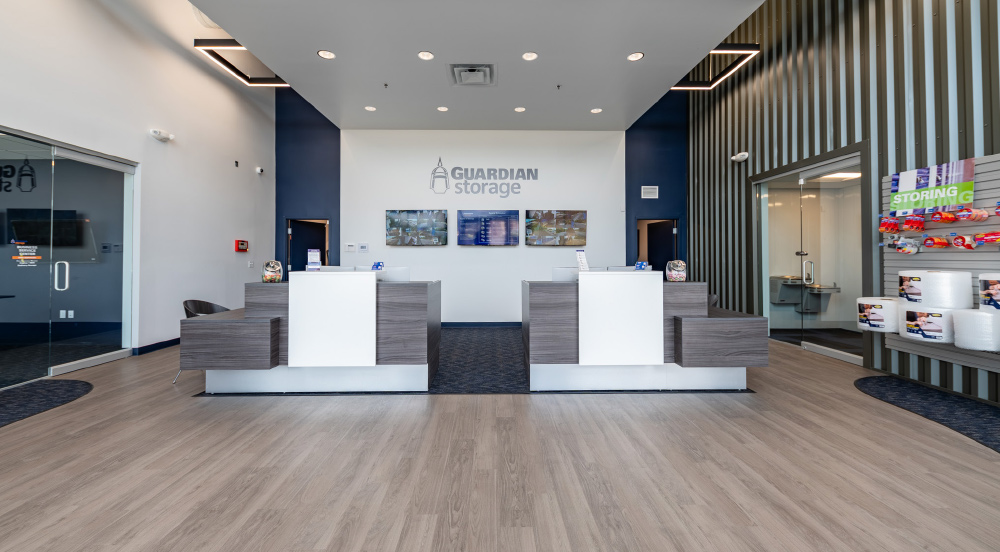 A modern, brightly lit self-storage lobby (Guardian Storage) with two counters and a retail area