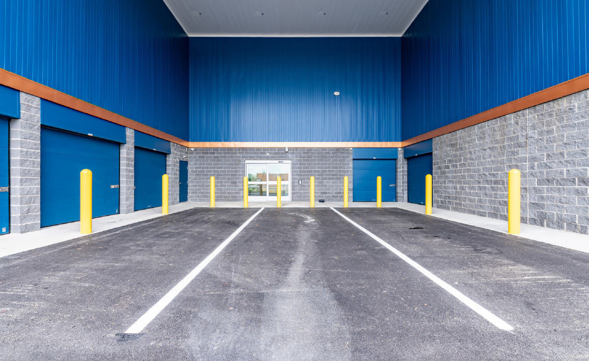 Covered loading area with blue walls, yellow bollards, and drive-up storage doors.