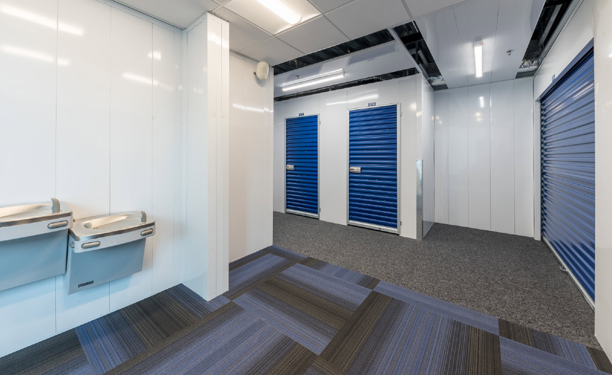 Indoor storage hallway with blue doors, patterned carpet, and water fountains on the left.