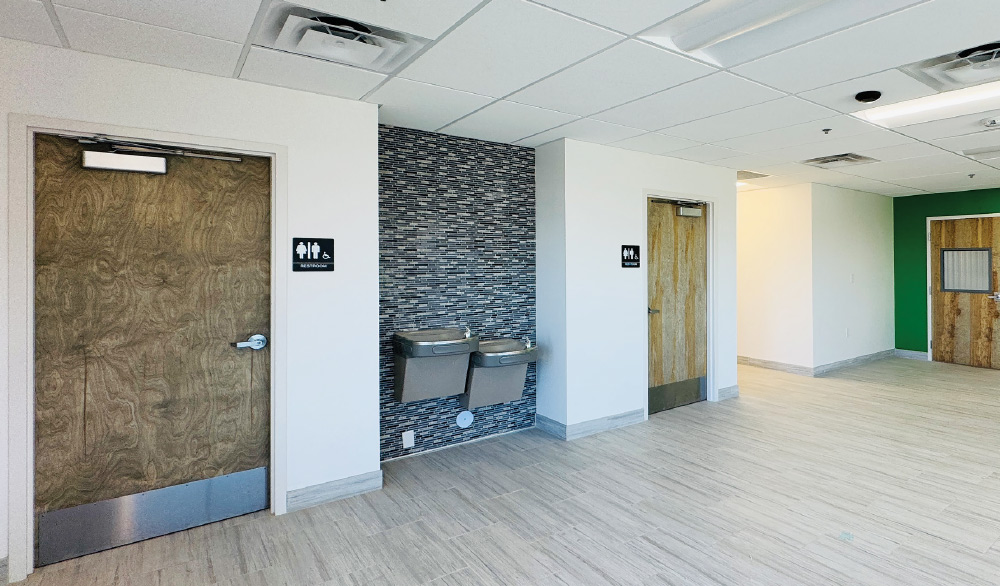Interior hallway with restrooms, water fountain with stone tile, and wood-grain doors.