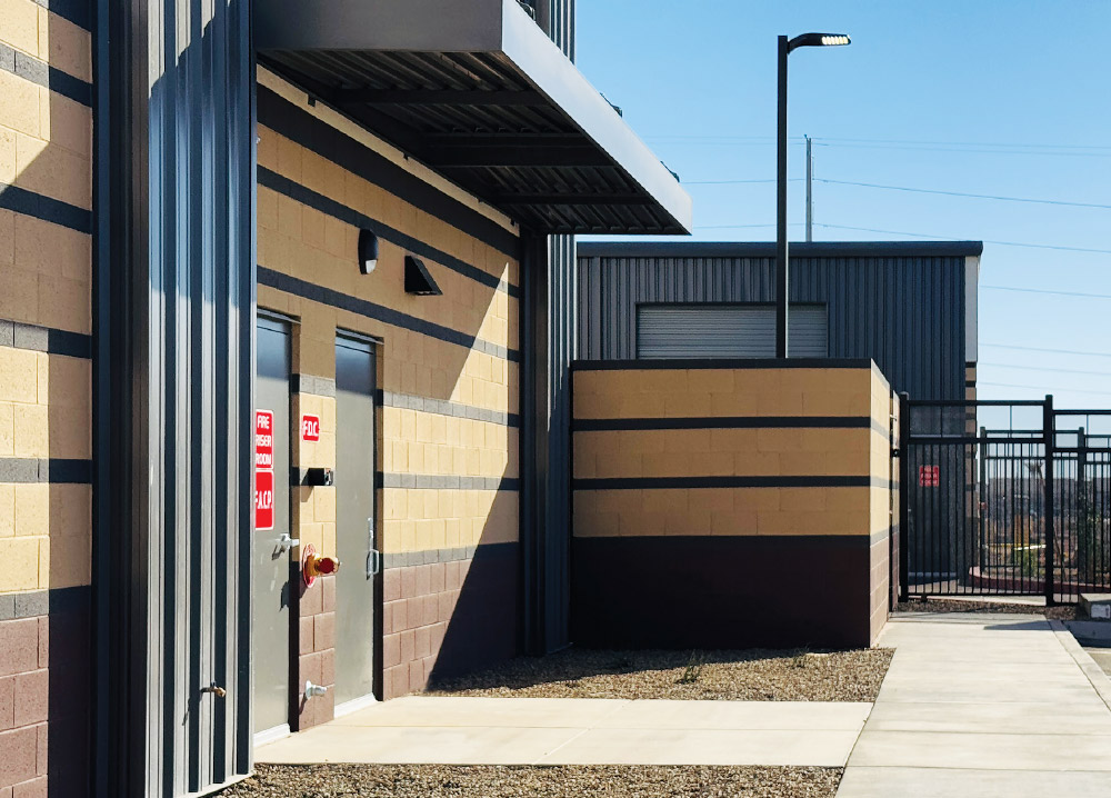 Side view of an exterior storage building with striped walls, metal siding, and a fenced gate.