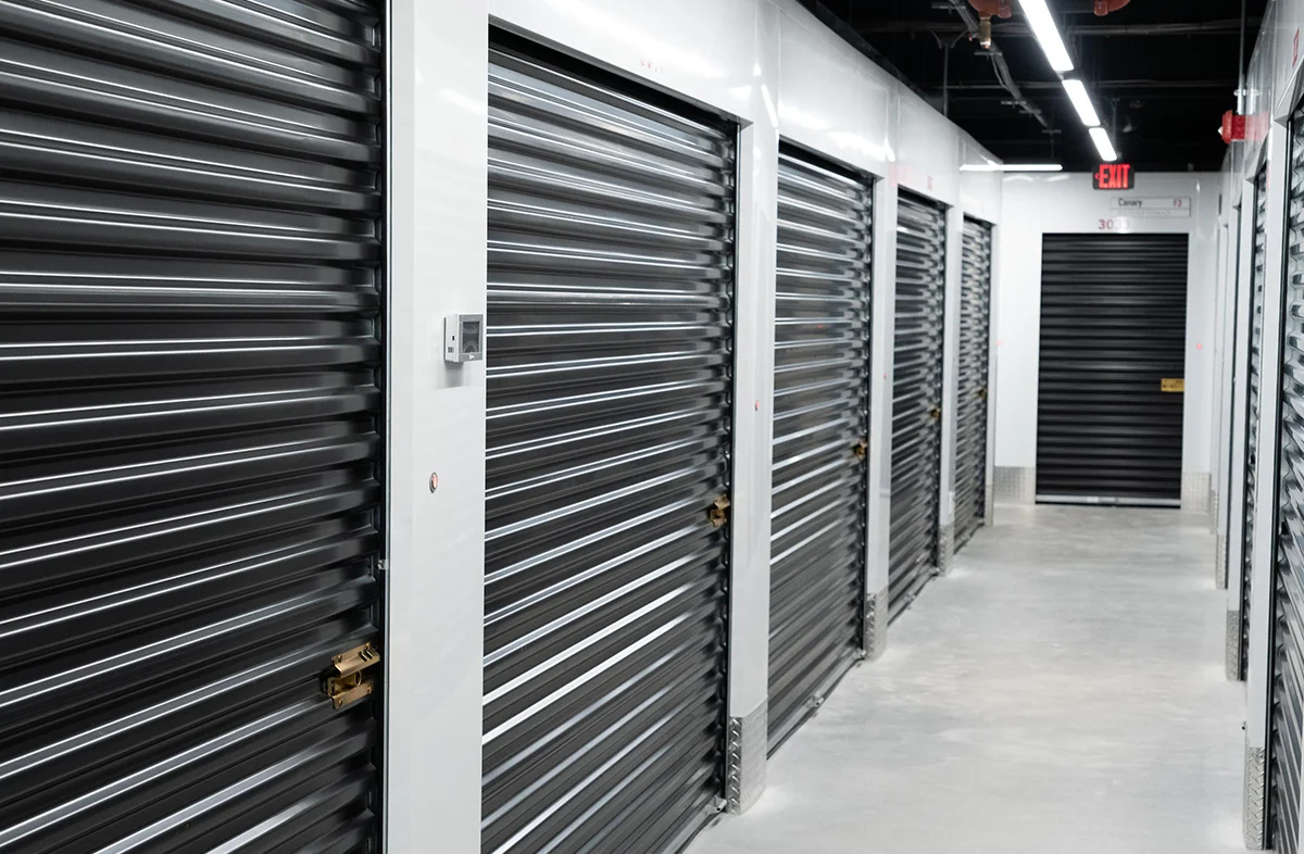 Secure storage unit aisle with contemporary design, bright lighting, and an exit sign visible at the end of the row.