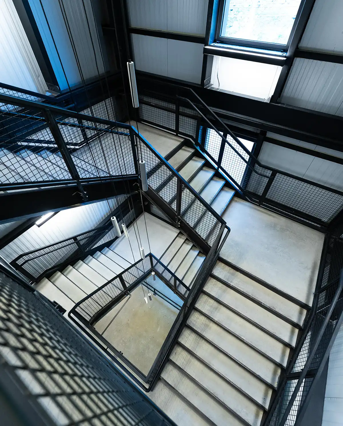 High-angle view of a modern industrial staircase with black metal grating and railings in a multi-story commercial building.