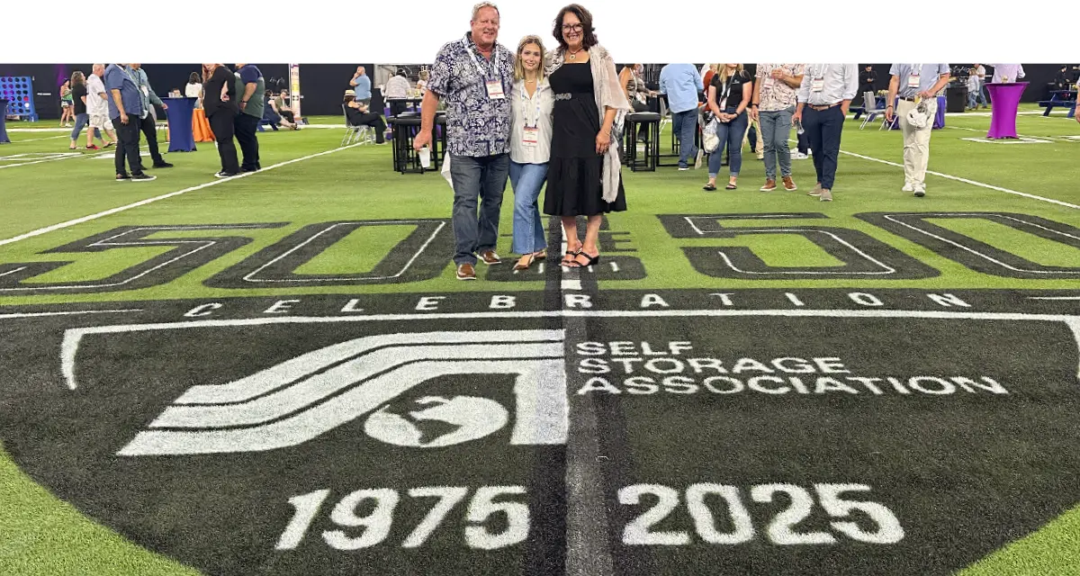 Three people standing on a turf field featuring the Self Storage Association Celebration logo, spanning the years 1975 to 2025