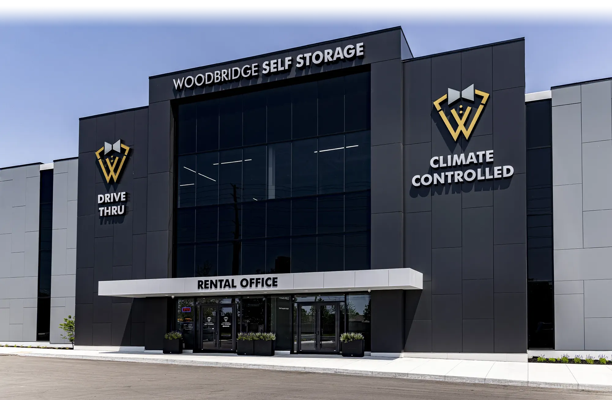 A modern, dark gray and black commercial building labeled "Woodbridge Self Storage" and "Climate Controlled" with a prominent "Rental Office" entrance and "Drive Thru" labeling.