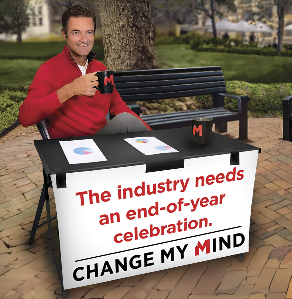 A man in a red sweater holds a mug at a table with charts and a sign that reads "The industry needs end-of-year celebration."