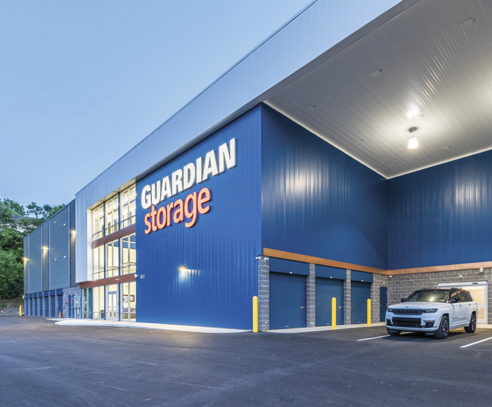 Blue storage facility with "GUARDIAN storage" sign and parked SUV.