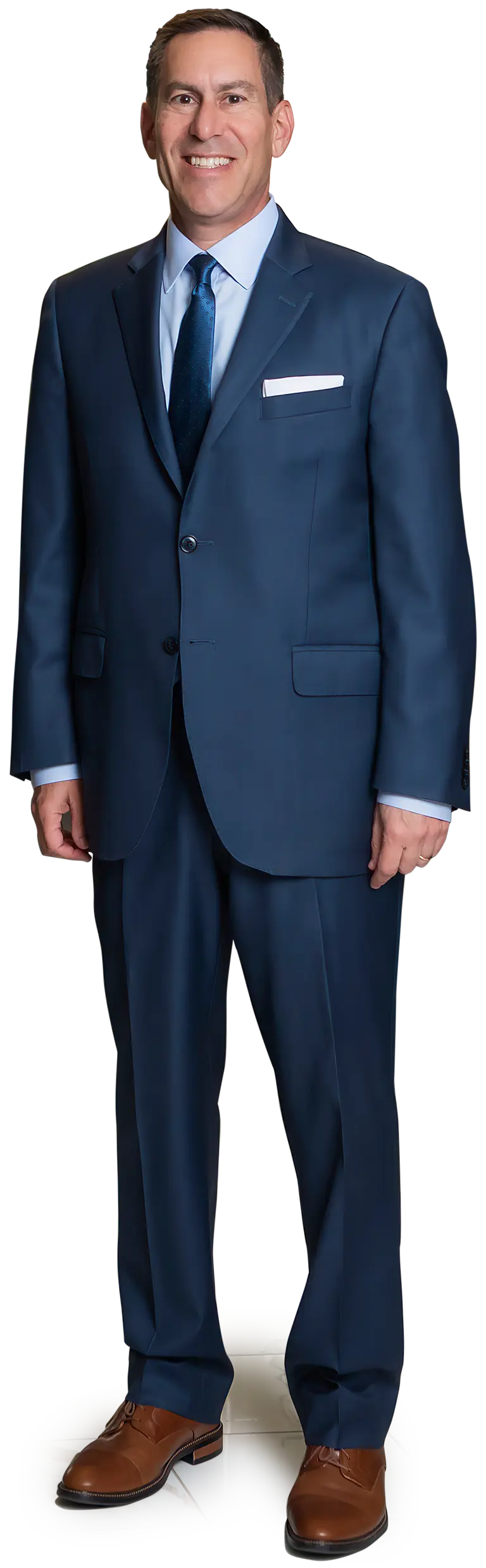 Full-length body shot picture of Scott I. Zucker, a smiling man wearing a tailored dark navy blue suit over a light sky blue button-up dress shirt with a dark blue tie and a white pocket square; He is wearing brown dress shoes and posing with his hands at his sides