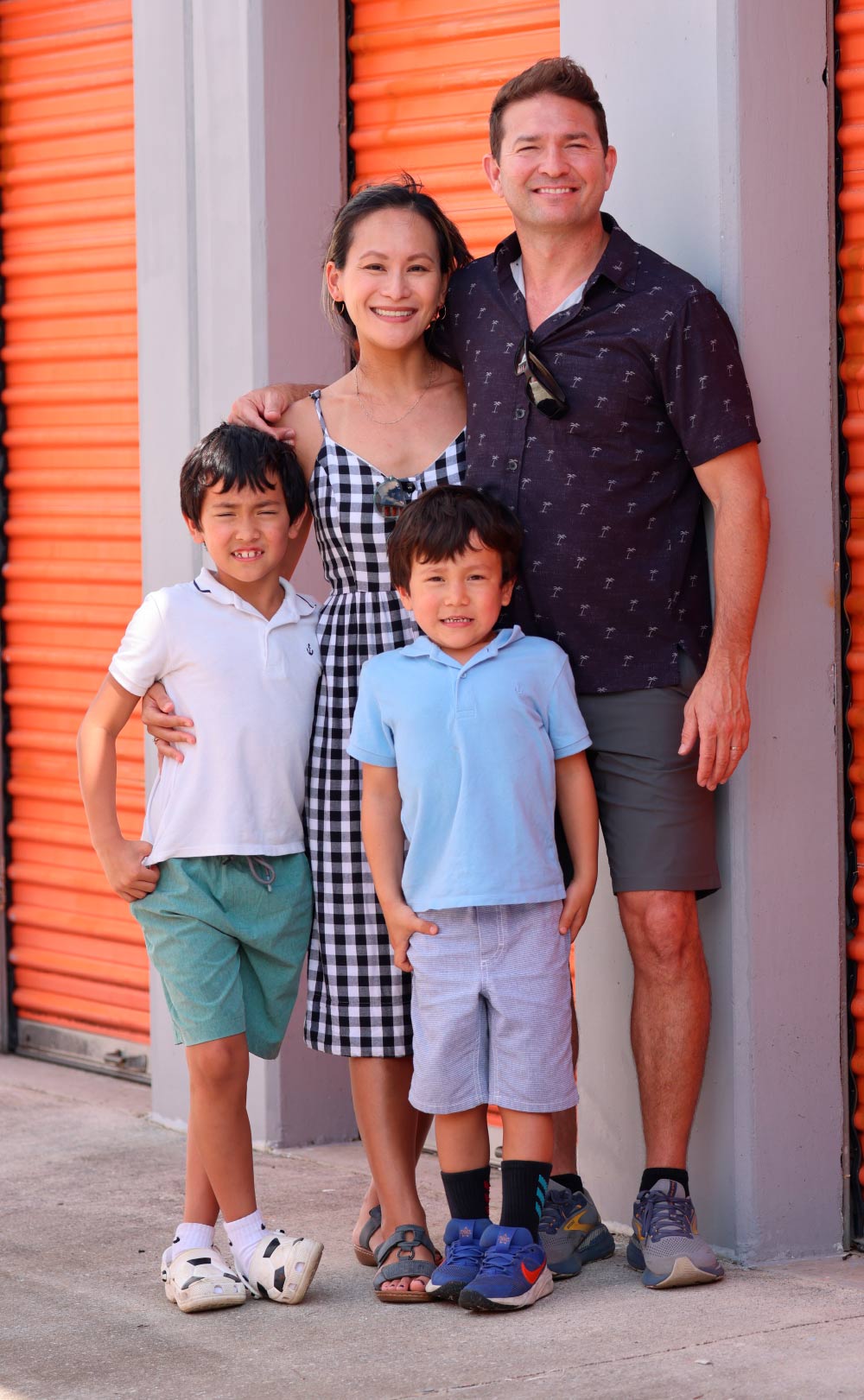 A smiling family of four posing together in front of orange self-storage unit doors.