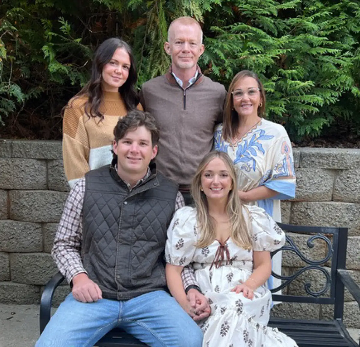 A smiling family of five posing together outdoors in front of lush green trees, featuring Shannon James and her family members.