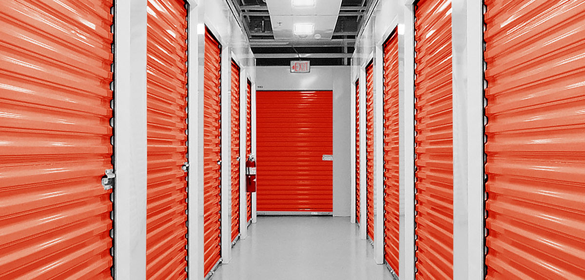 Interior view of a clean storage facility hallway with bright orange unit doors and white trim.