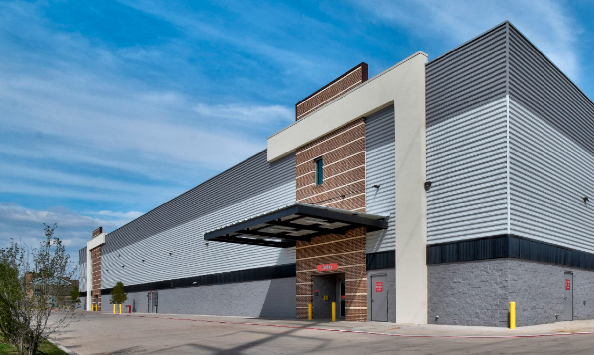 Low-angle exterior shot of a large, multi-toned gray industrial storage building with a brick-accented loading bay entrance.