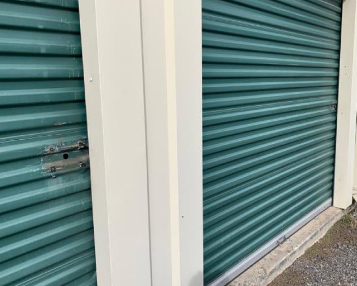 Close-up of two green corrugated metal roll-up doors at a self-storage facility, showing the cream-colored trim and a sliding latch mechanism