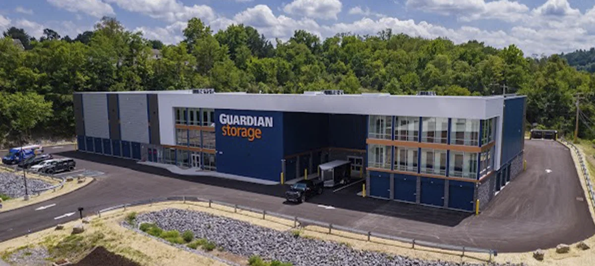 An aerial view of a large, multi-story Guardian Storage facility featuring modern blue and white architecture, climate-controlled units, and wide paved driving lanes for easy access