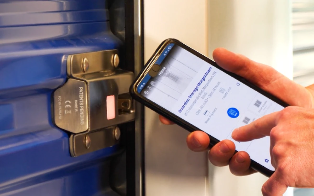 A customer using a smartphone app to wirelessly unlock a blue electronic smart lock on a Guardian Storage unit door, demonstrating keyless entry technology