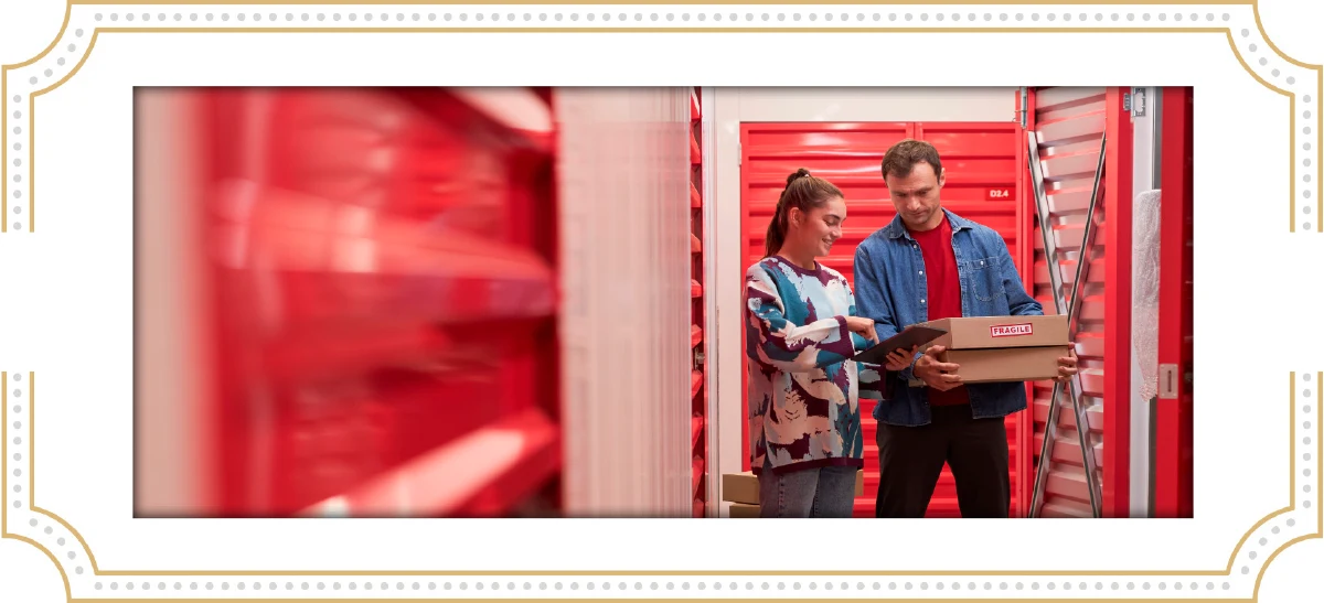 A man and woman reviewing a digital inventory on a tablet while standing in front of red climate-controlled storage units