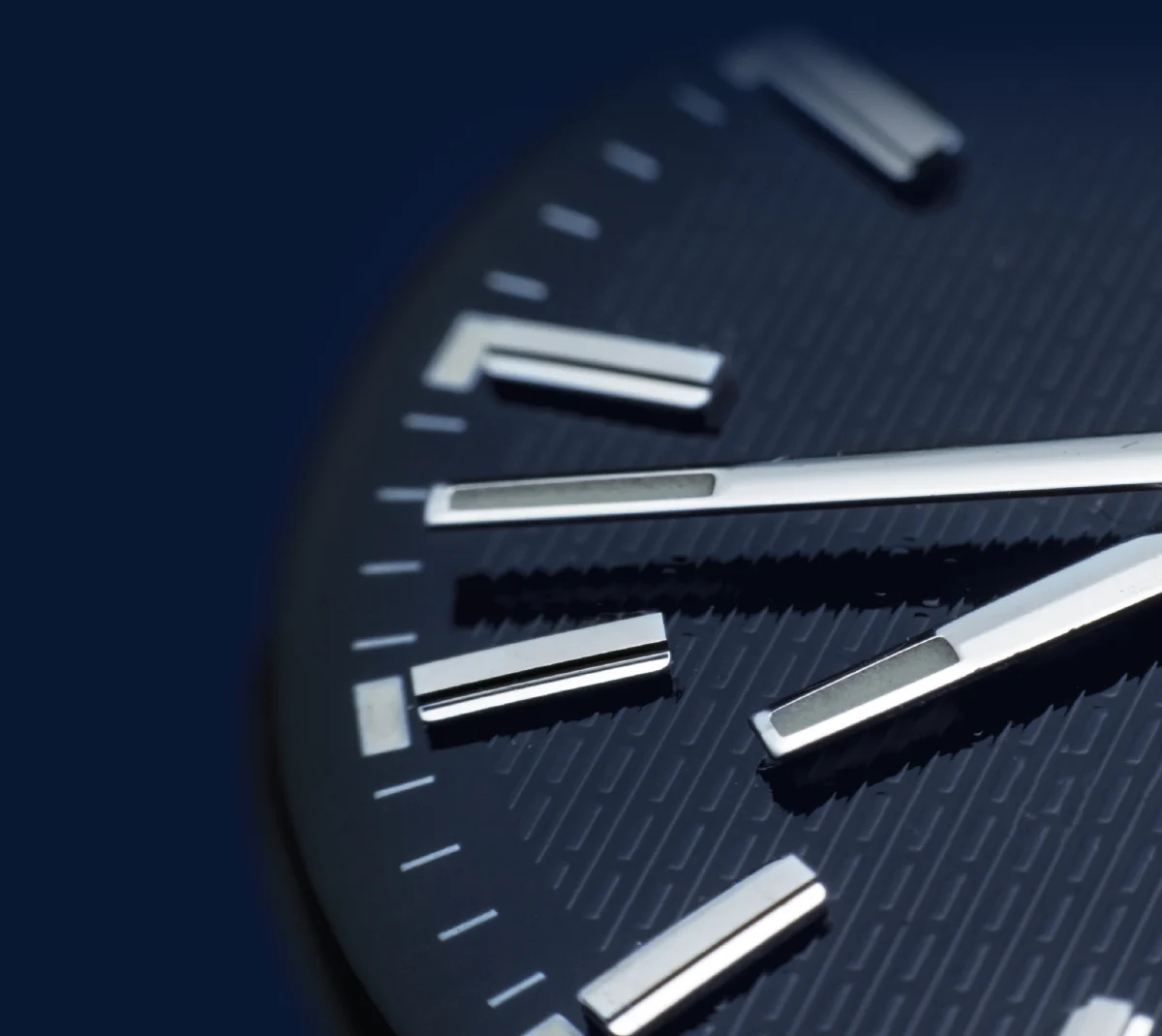 A close-up, angled view of a modern watch dial with polished silver markers and minute hands