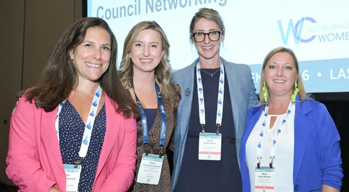 Four smiling women (Jessica Lamoureux, Anna Dwyer Bennet, Kristi Adams, and Stacie Maxwell) stand together at a professional networking event, wearing conference lanyards in front of a presentation screen that reads Council Networking and features the Self Storage Women logo