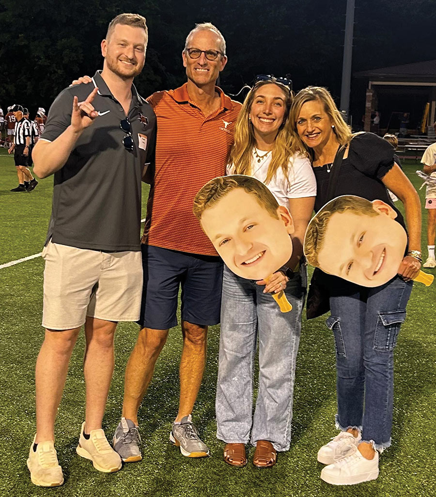 Noah Starr with his family on field holding large signs of his head