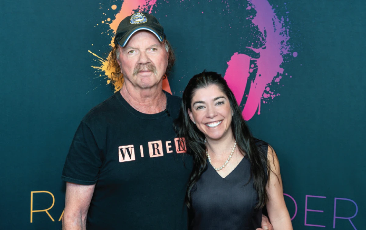 Radio host Harry Wilder and a guest posing in front of a dark teal backdrop featuring the colorful splash-style Radio Wilder logo and headphones graphic