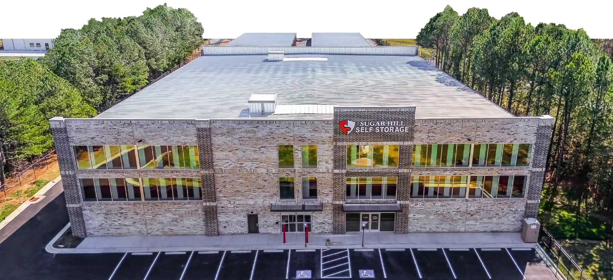 Aerial view of a large, modern multi-story brick self-storage facility with the "Sugar Hill Self Storage" logo.