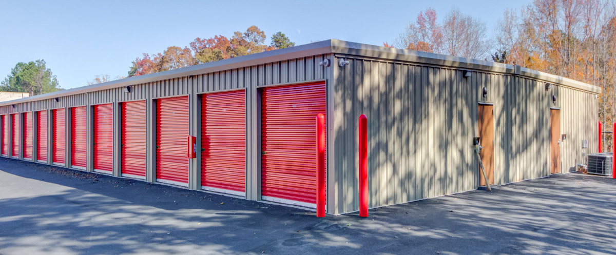 Exterior row of outdoor self-storage units with bright red roll-up doors and tan metal siding.