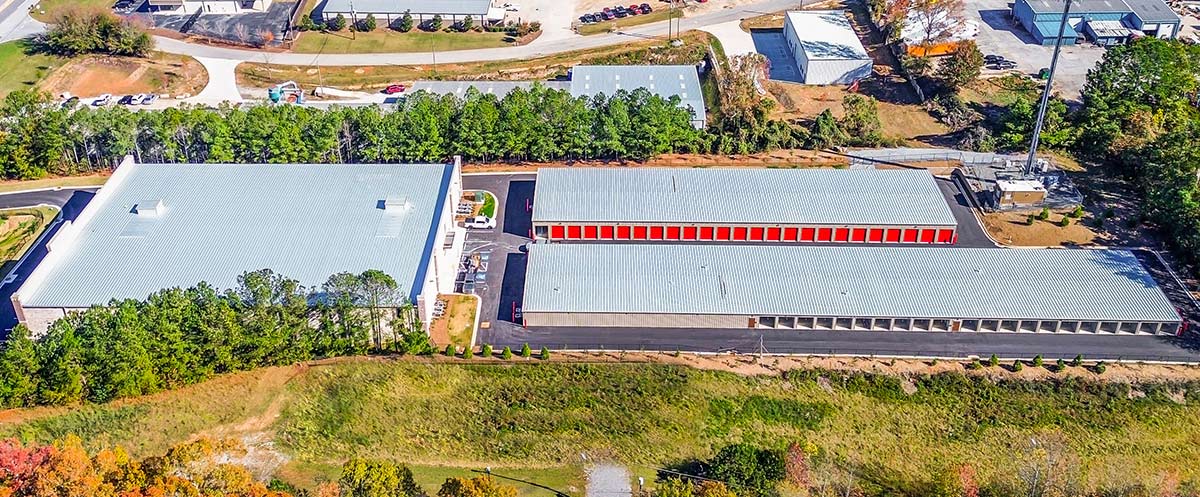 High-angle aerial view of a storage facility complex featuring several long metal buildings and a paved parking area