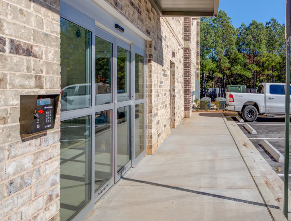 Close-up of a glass sliding door entrance to a storage facility with a wall-mounted digital keypad for secure access.