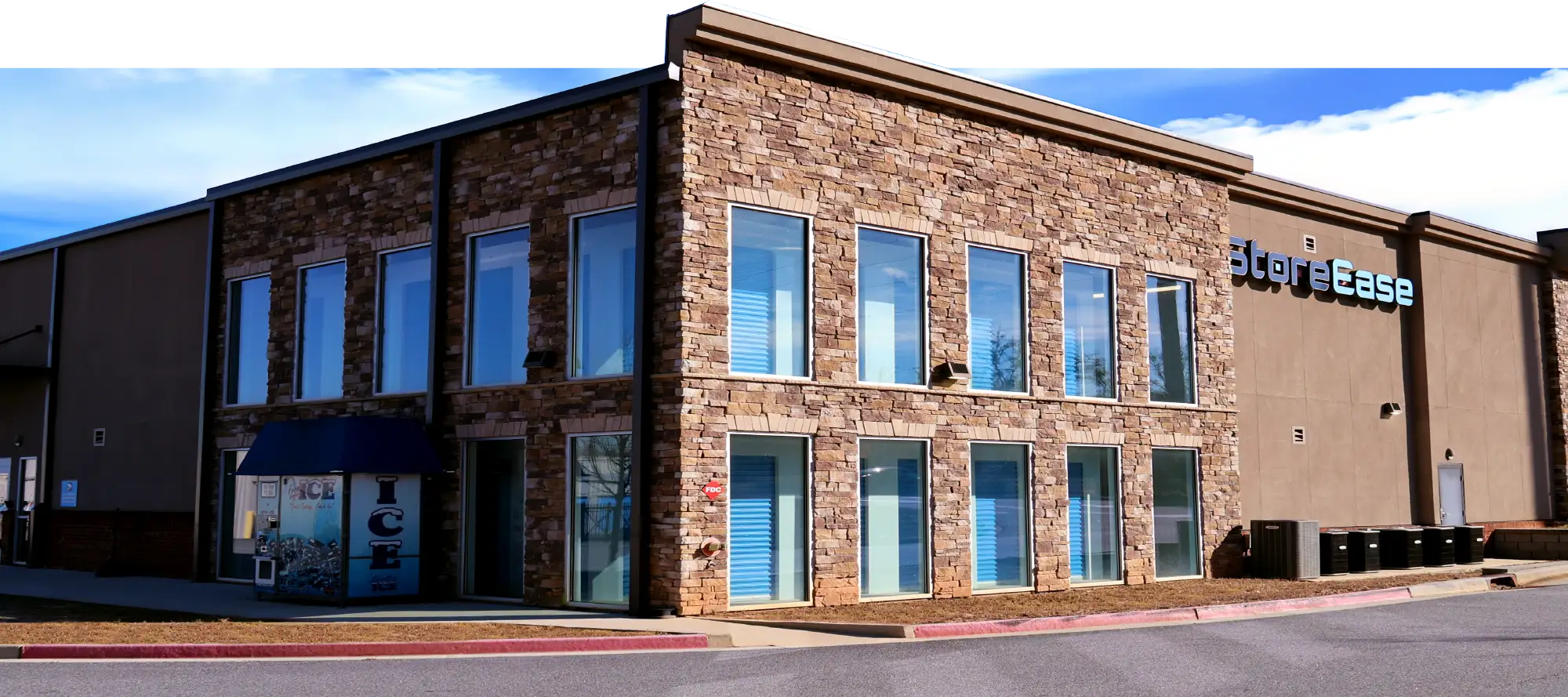 Exterior of a modern StoreEase self-storage facility with a stone facade, large windows, and an onsite ice vending machine.