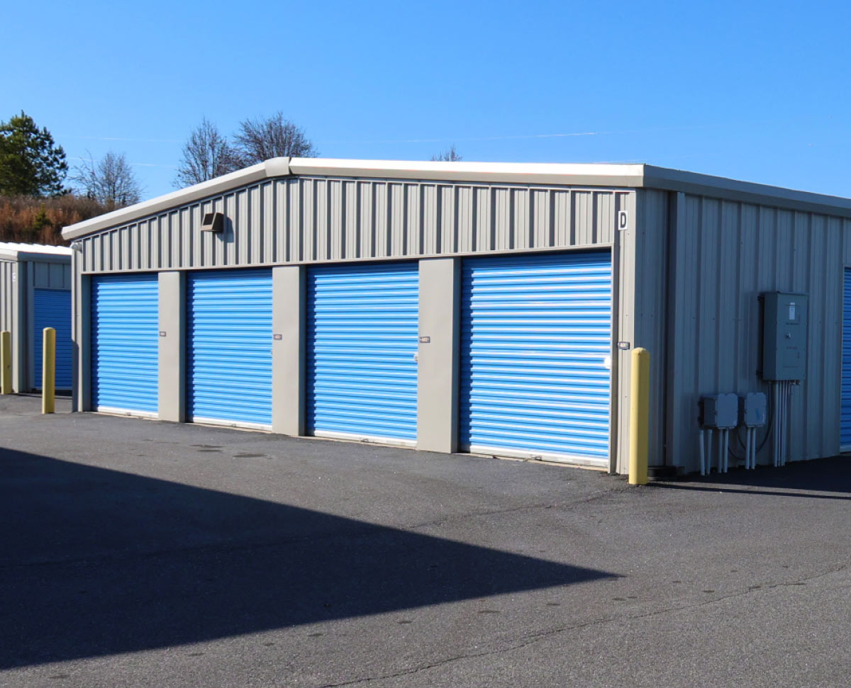 Exterior row of drive-up self-storage units with blue metal doors at a StoreEase facility under a clear blue sky.