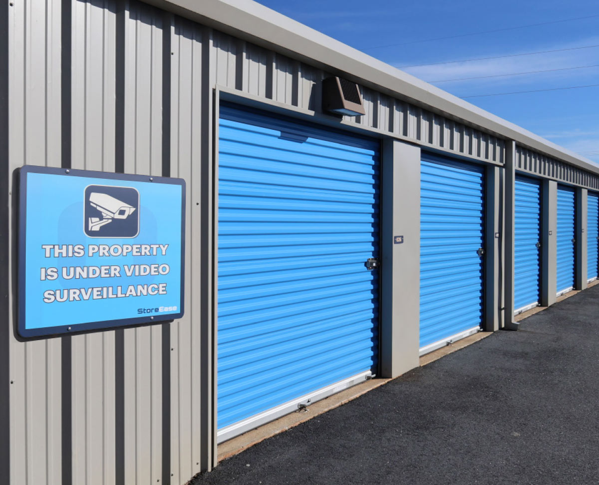 Exterior storage units with blue doors and a sign stating the property is under video surveillance by StoreEase.