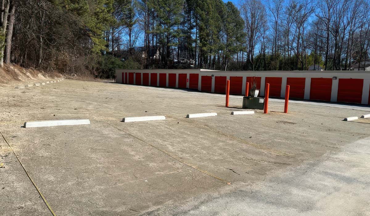 White parking bumpers installed on a level grey base at a self-storage facility, preparing for the final layer of asphalt maintenance.