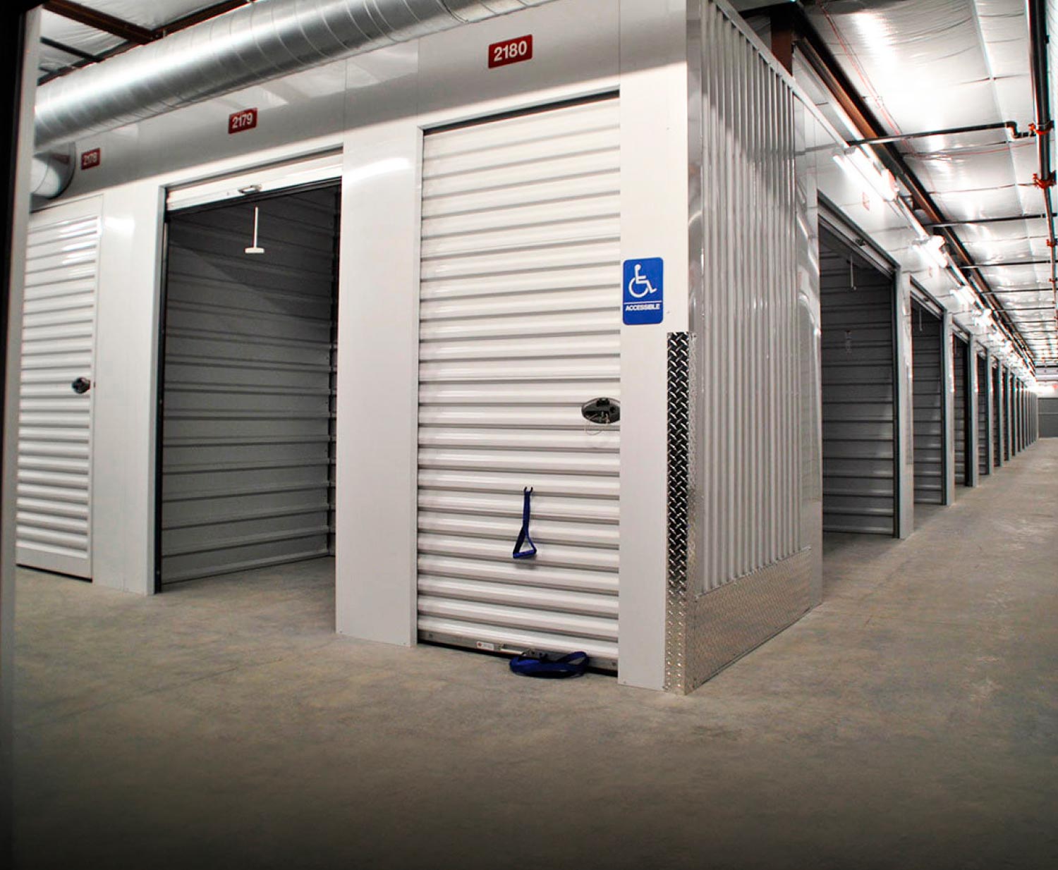 Interior view of a self-storage facility with white doors, featuring a blue ADA-accessible unit sign and pull-down strap.