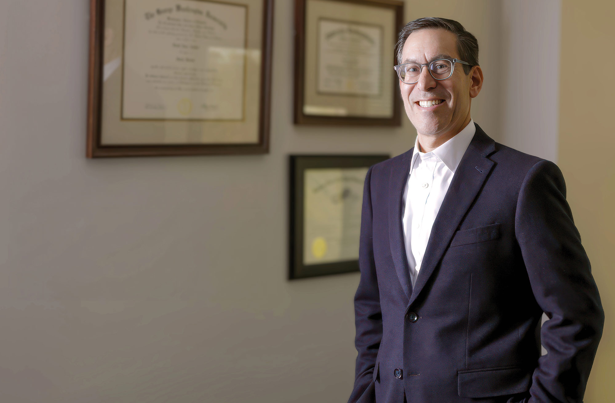A professional portrait of a smiling Scott Zucker standing in an office.