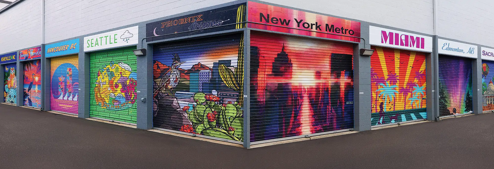 A row of outdoor storage unit roll-up doors, each painted with vibrant, custom city-themed murals.