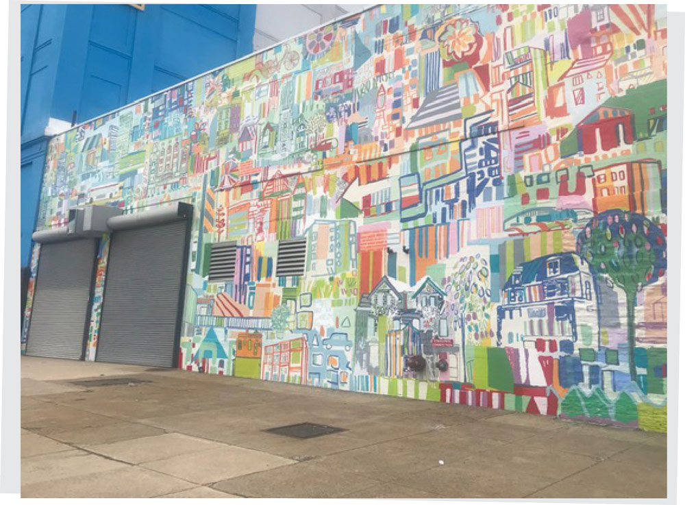 A massive, highly detailed and colorful cartoon-style street mural painted across a large brick building wall.