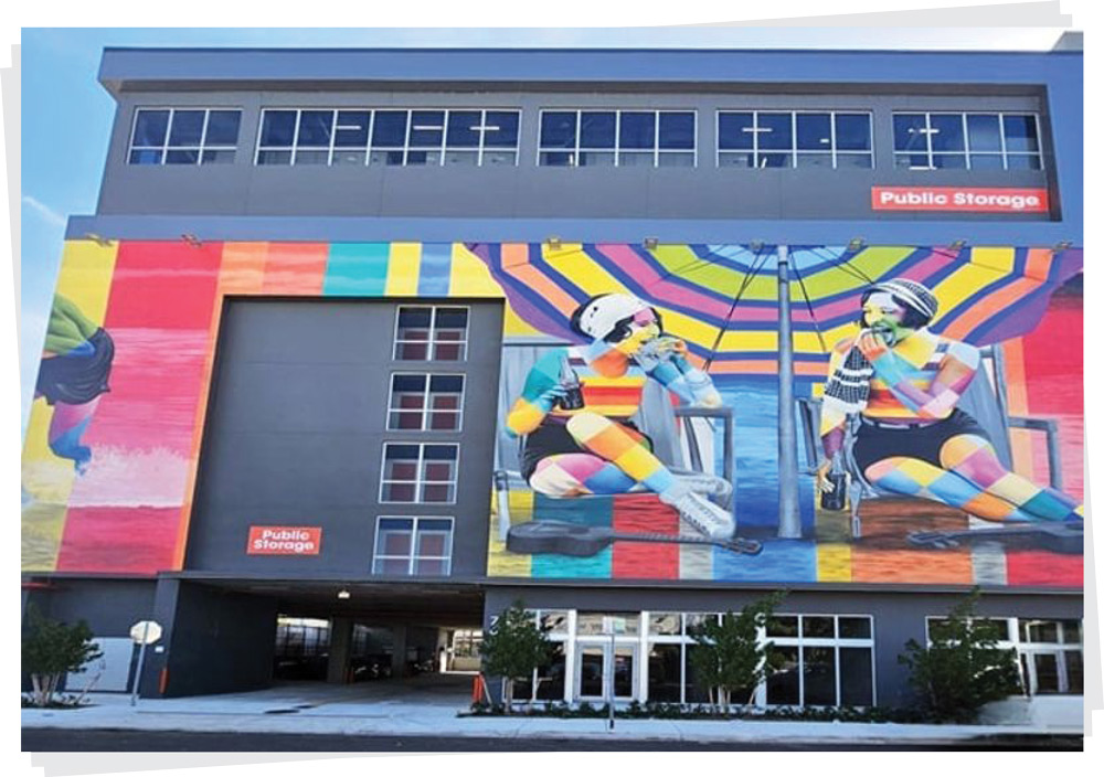A multi-story Public Storage building featuring a massive, vibrant mural of people relaxing at a beach.