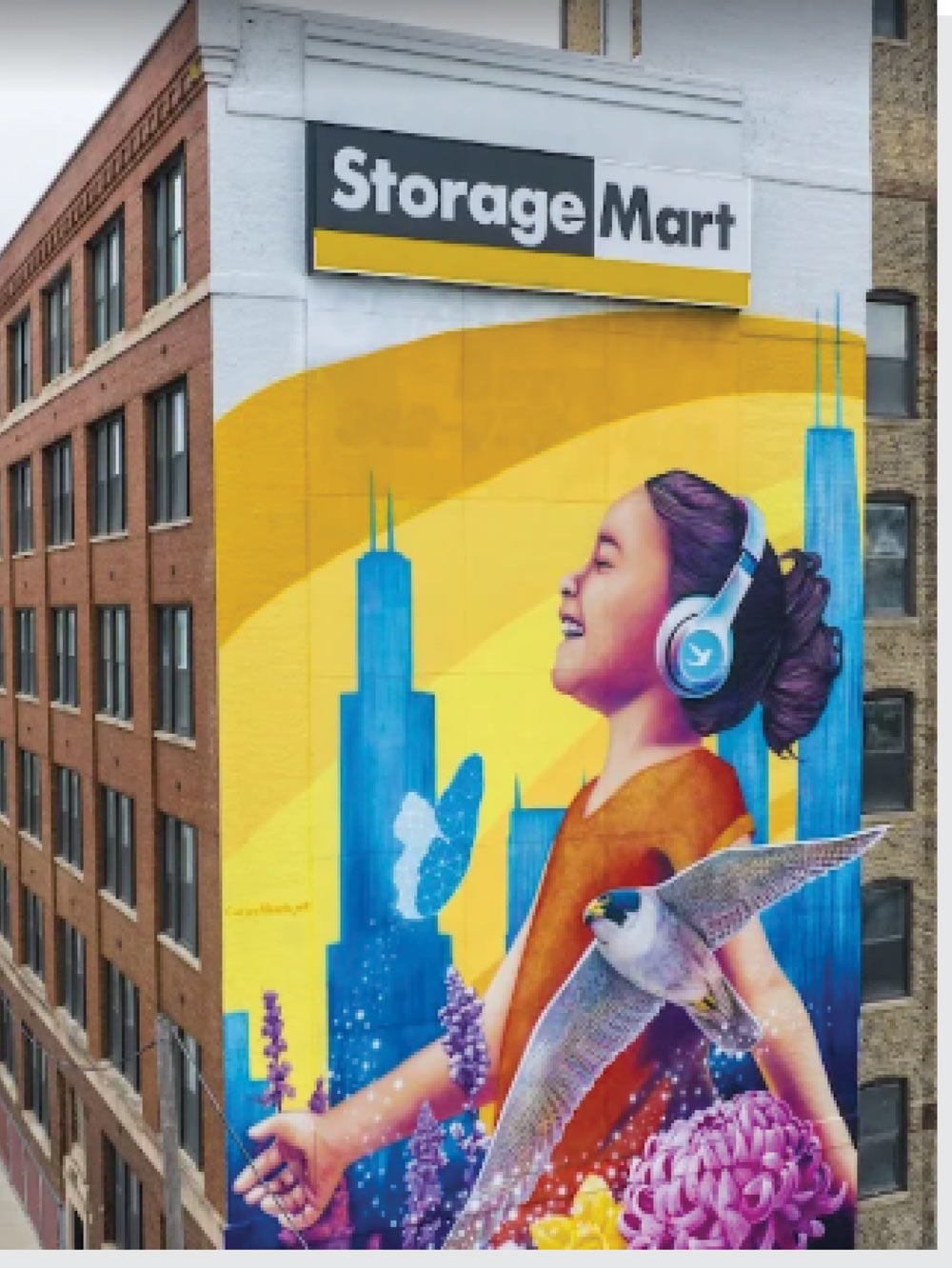 A large building mural for Storage Mart depicting a smiling girl wearing headphones against a city skyline.