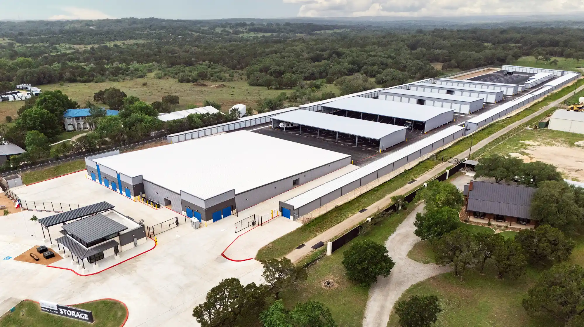 An aerial view of a large, modern self-storage facility featuring enclosed buildings and covered RV parking stalls surrounded by trees.