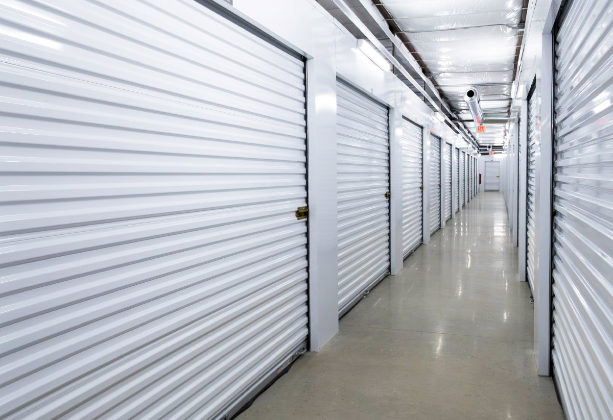 A long, brightly lit interior hallway lined with clean, white roll-up doors for individual climate-controlled storage units.
