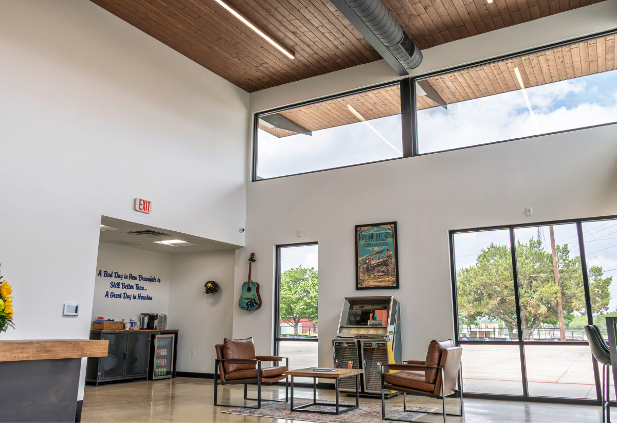 A spacious lobby lounge featuring leather armchairs, a wooden ceiling, large windows, an old-school jukebox, and a hanging guitar.