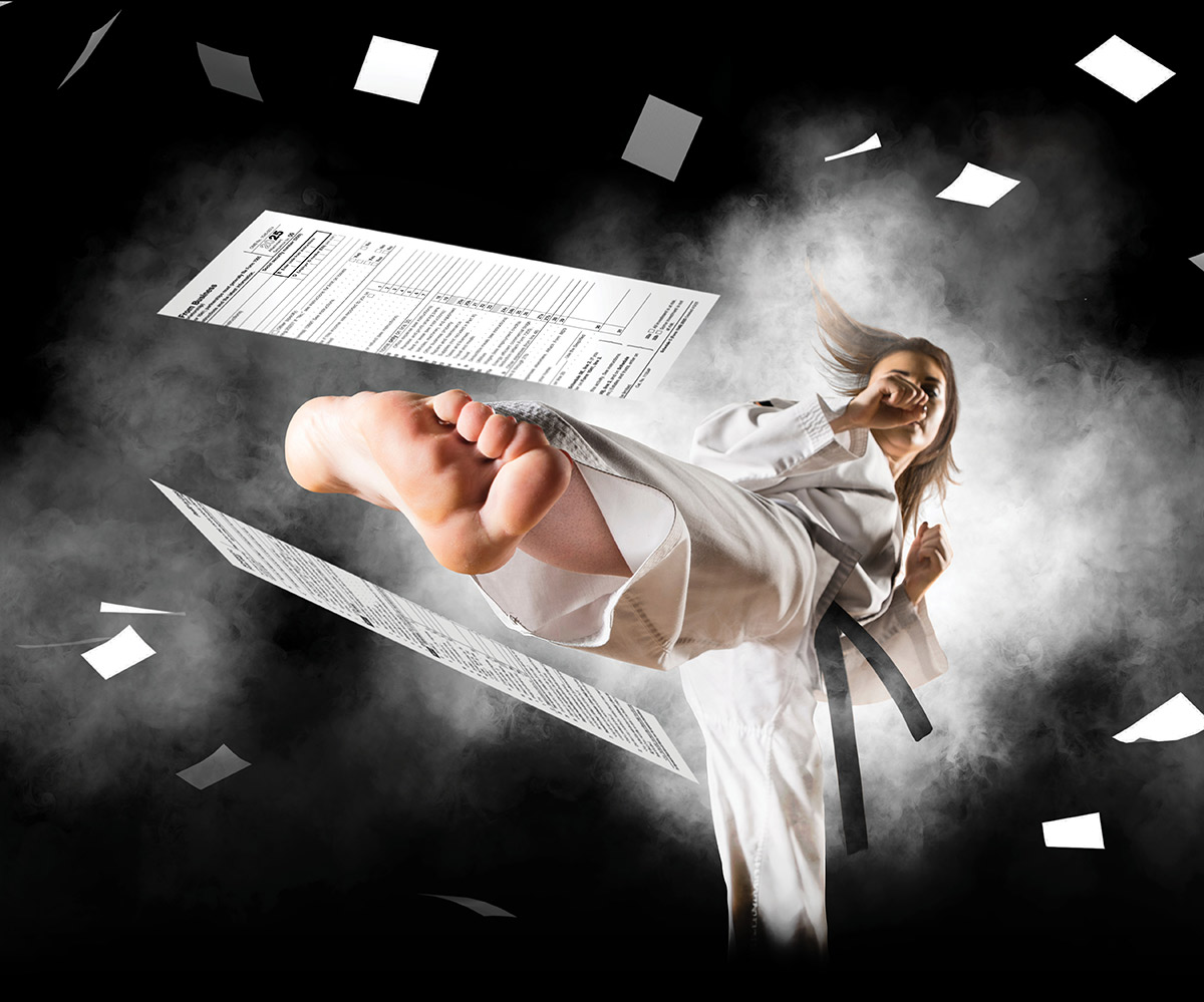 A martial artist in a white uniform and black belt executes a high kick toward the camera, sending tax forms and papers flying against a smoky black background.