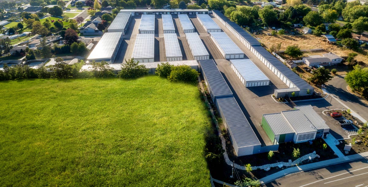 An aerial view of a large, sprawling outdoor self-storage facility with long rows of metal units next to a vibrant green field.