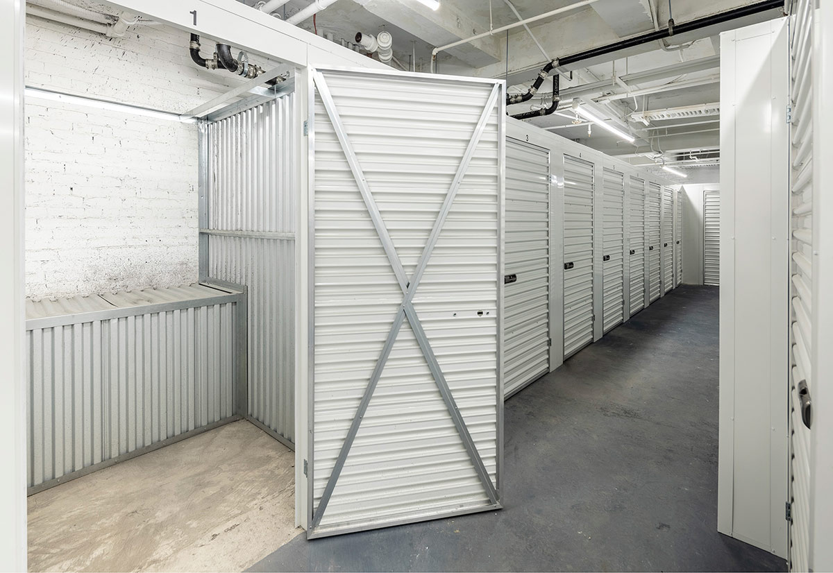 Indoor corridor of a Local Locker self-storage facility with a row of white corrugated metal doors, featuring one open locker showing an empty unit.