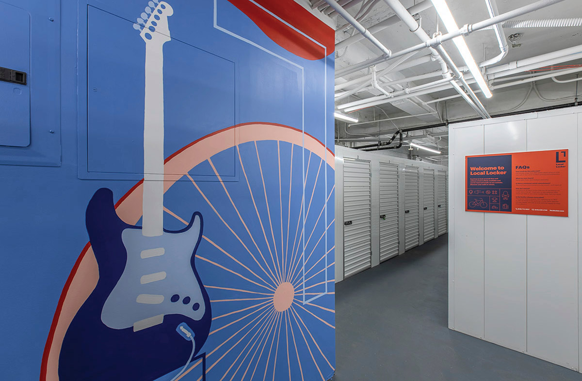 Interior hallway of Local Locker with a blue mural of an electric guitar and bicycle wheel on the left, and a row of white storage units in the background.