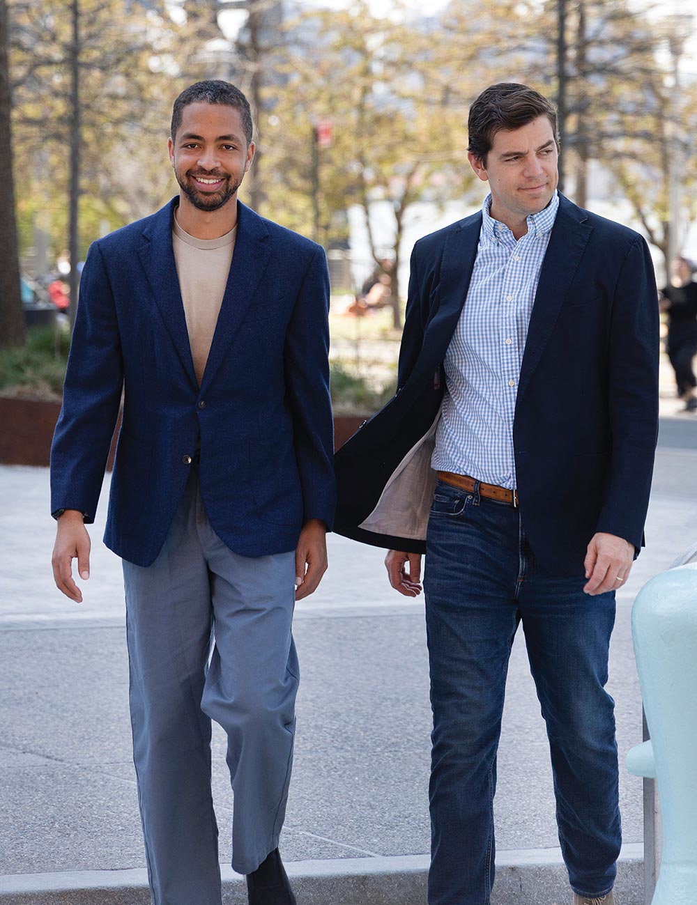 Alex Hartman and Peter Smyth walking side-by-side outdoors on a paved public walkway.