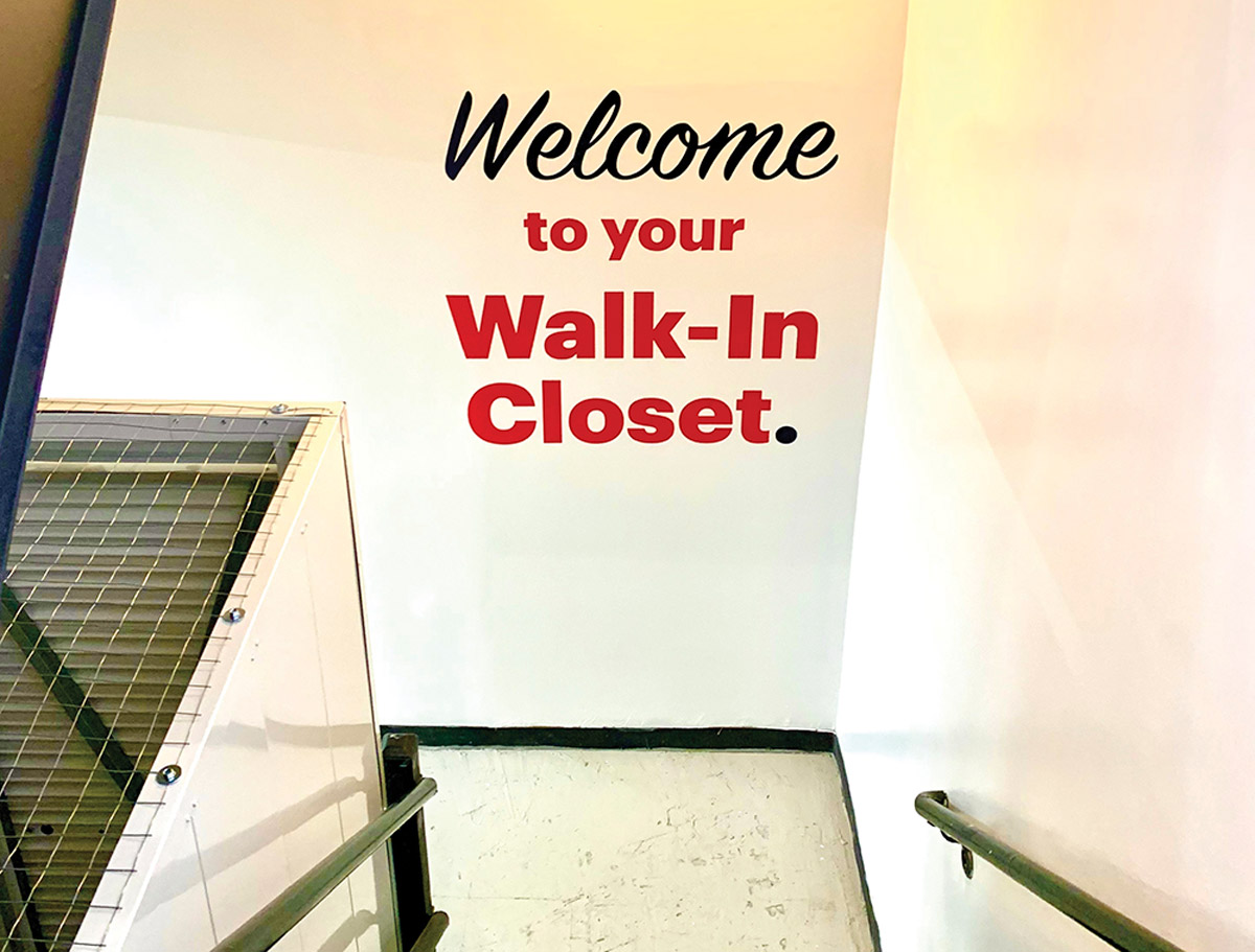 Looking down a white stairwell managed by White Label Storage, with a wall sign reading "Welcome to your Walk-In Closet."