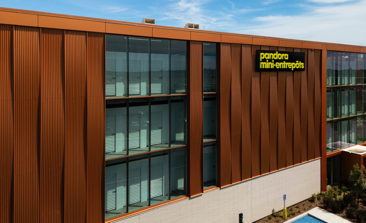 Modern multi-story Pandora self-storage building featuring bronze-colored metal siding, large glass windows, and a yellow sign.