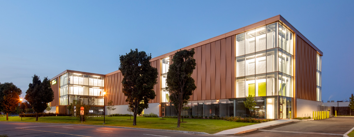 Wide shot of the Pandora self-storage facility at twilight, showing illuminated interior storage units through large glass corner windows.